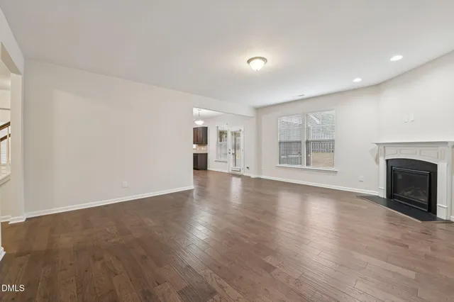 an empty room with wooden floor fireplace and windows