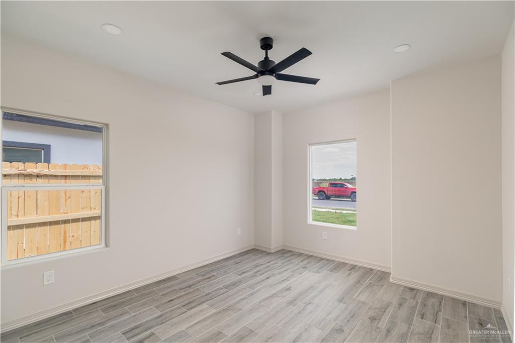 2118 Trinity Street Donna, TX 78537 - Photo 6 of 13 an empty room with wooden floor a ceiling fan and windows