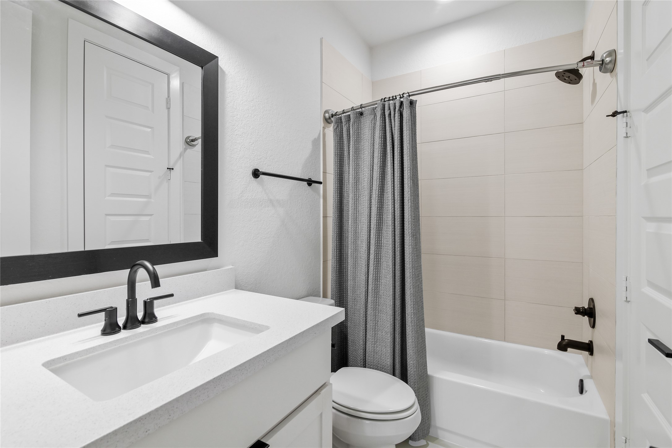 4231 Allen Street Houston, TX 77007 - Photo 14 of 31 This modern en suite pairs white shaker cabinets and quartz counters with bold matte black hardware for a high-contrast look. Warmth is added through large-format, sand-beige shower tiles laid in a clean horizontal pattern.
