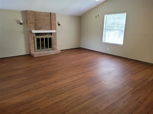 an empty room with wooden floor fireplace and windows