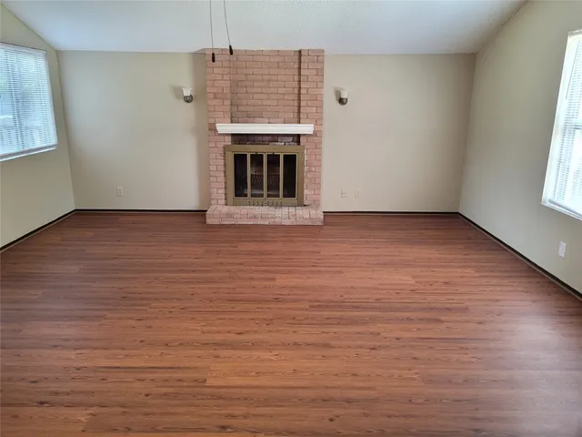 a view of an empty room with wooden floor fireplace and a window