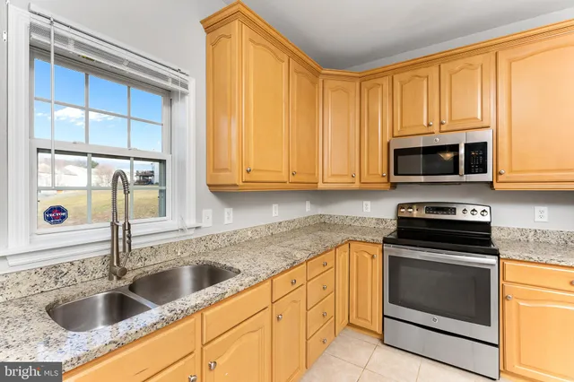 a kitchen with granite countertop a sink stainless steel appliances a stove a microwave and cabinets
