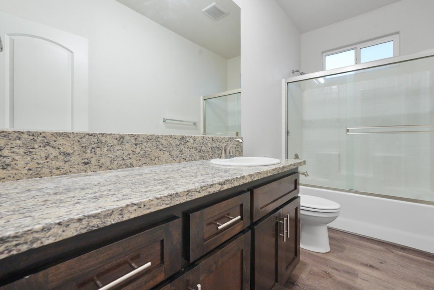 683 Granada Court Merced, CA 95341 - Photo 7 of 9 a bathroom with a granite countertop sink a toilet a mirror and shower