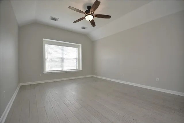 an empty room with wooden floor ceiling fan and windows
