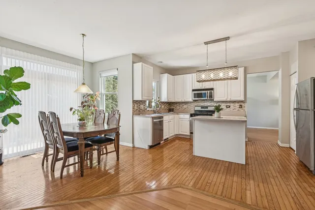 a kitchen with granite countertop stainless steel appliances a dining table chairs stove refrigerator and cabinets