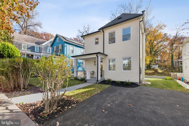 a view of a white house next to a yard with big trees and plants