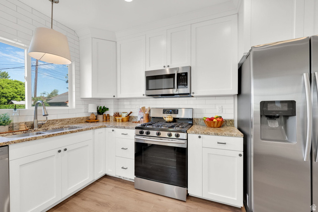 446 South 300 East Provo, UT 84606 - Photo 15 of 32 Modern kitchen featuring white cabinetry, granite-style countertops, stainless steel appliances, a subway tile backsplash, and wood-finish flooring