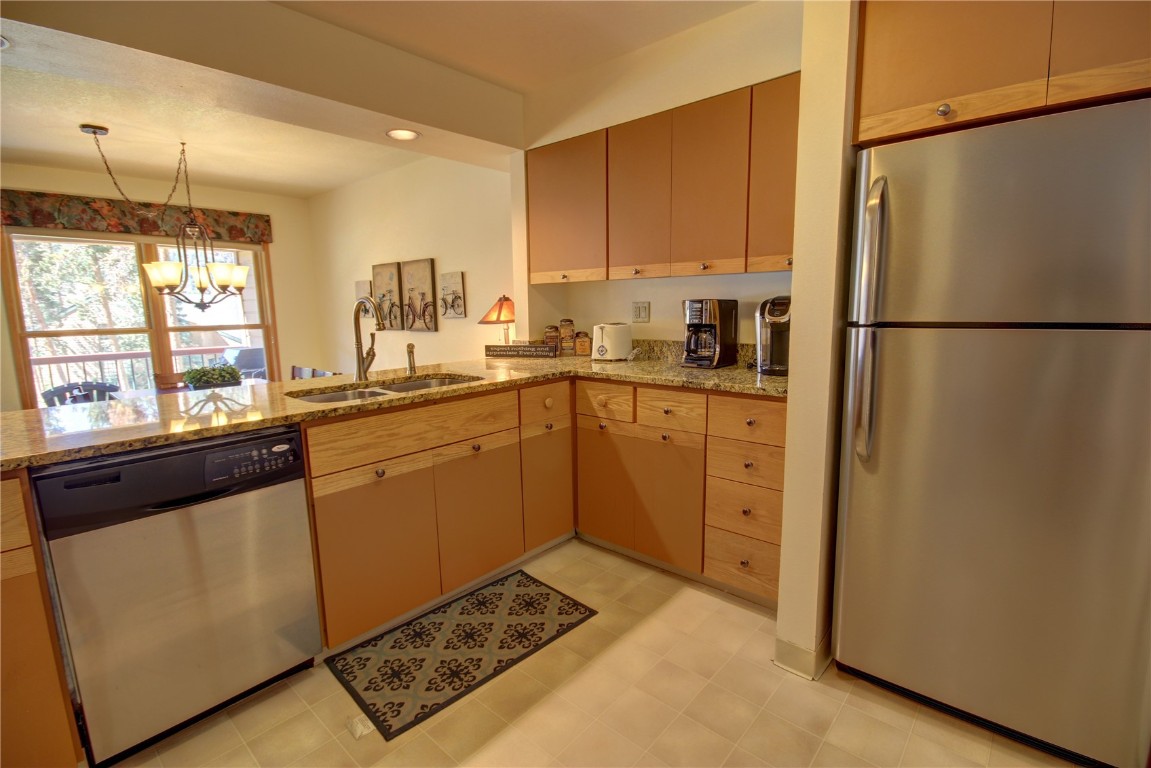 Kitchen featuring stainless steel appliances, light stone counters, kitchen peninsula, a notable chandelier, and sink