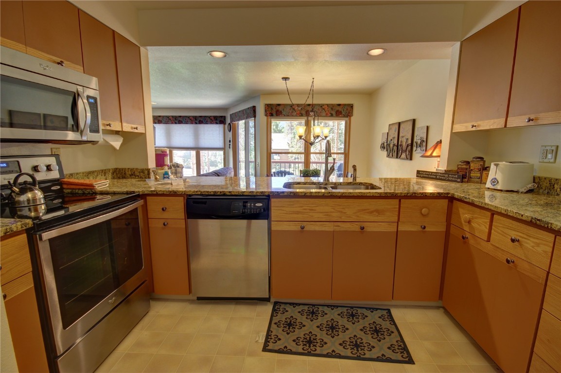 Kitchen with kitchen peninsula, appliances with stainless steel finishes, a notable chandelier, and sink