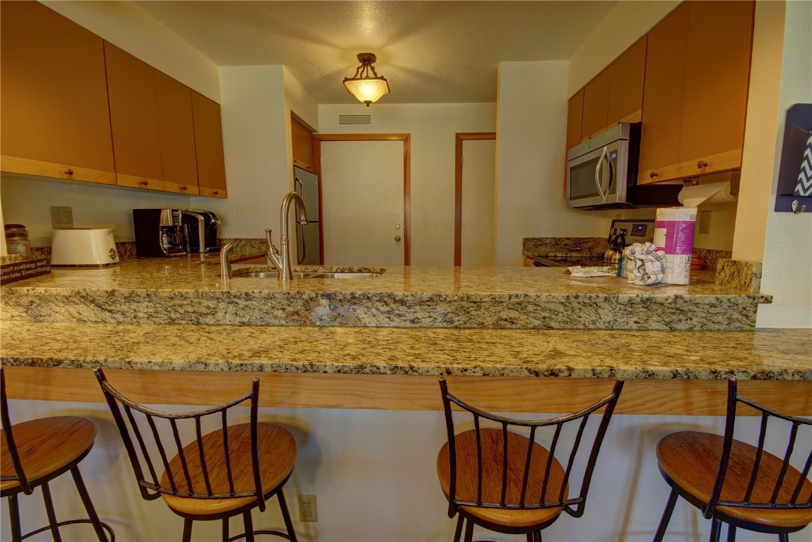 Kitchen featuring kitchen peninsula, sink, a kitchen breakfast bar, electric range, and light stone countertops