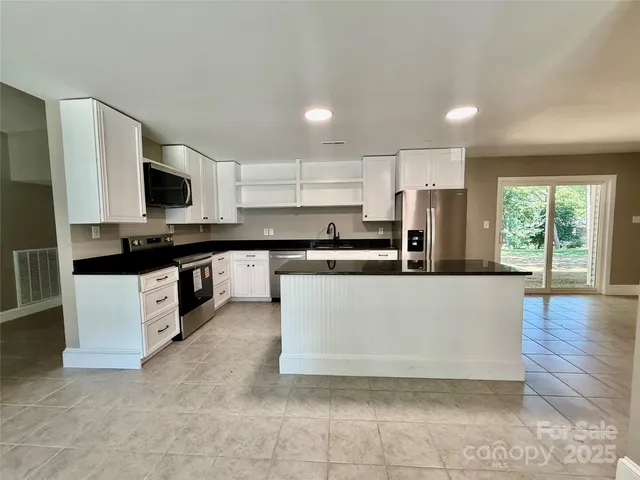 a large kitchen with stainless steel appliances a stove a sink a microwave a refrigerator and white cabinets with wooden floor