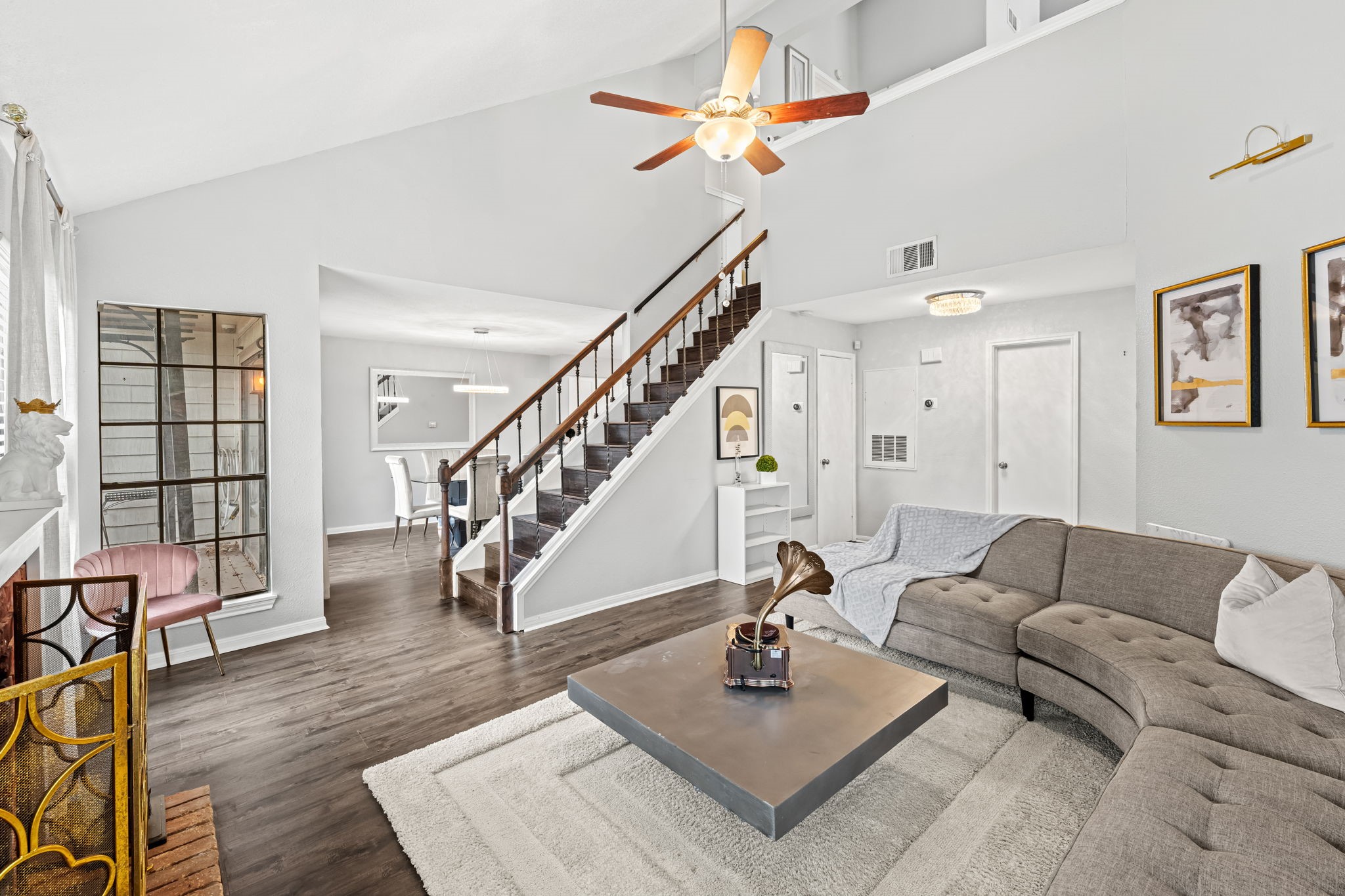 2211 South Kirkwood Road, Unit 1 Houston, TX 77077 - Photo 8 of 16 This wide view confirms what the first floor is actually delivering — a vaulted ceiling spanning the full combined length of the living and dining areas, with the dark wood staircase rising at center and the dining room's crystal ring pendant visible in the distance. The entry door and front of the unit are visible at the far end, communicating the full depth and openness of the layout in a single frame.