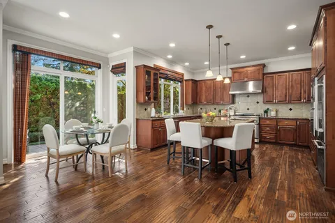 a kitchen with stainless steel appliances granite countertop a stove a refrigerator a kitchen island a dining table and chairs with wooden floor