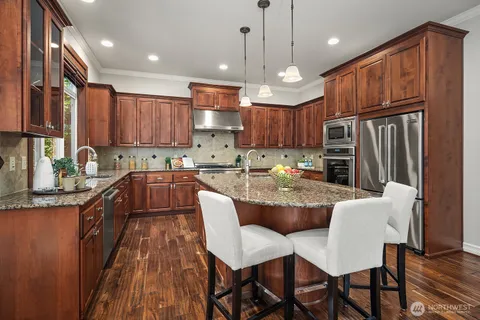 a kitchen with stainless steel appliances granite countertop a stove top oven a refrigerator a sink and chairs