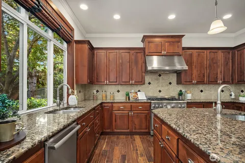a kitchen with stainless steel appliances granite countertop a sink a stove and a wooden cabinets