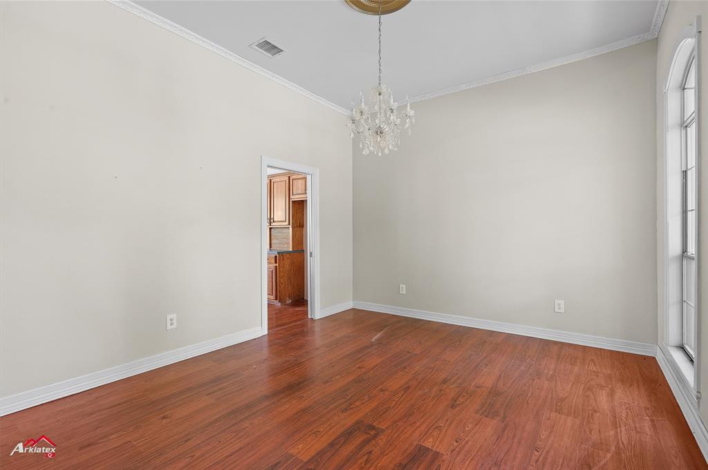 15280 Wynn School Road Hosston, LA 71043 - Photo 12 of 27 Empty room with crown molding, an inviting chandelier, baseboards, visible vents, and dark wood-style flooring