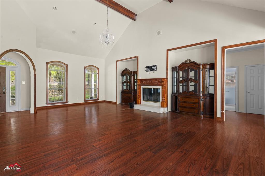 15280 Wynn School Road Hosston, LA 71043 - Photo 5 of 27 Unfurnished living room with high vaulted ceiling, a chandelier, beamed ceiling, wood finished floors, and a glass covered fireplace