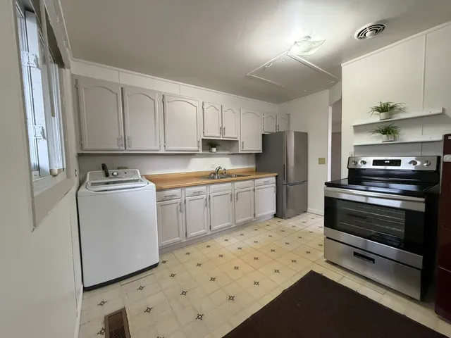 a kitchen with granite countertop a refrigerator sink stove and white cabinets