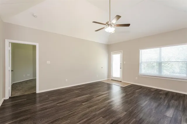 an empty room with wooden floor fan and windows