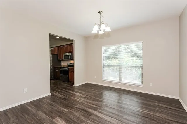 an empty room with wooden floor chandelier and windows