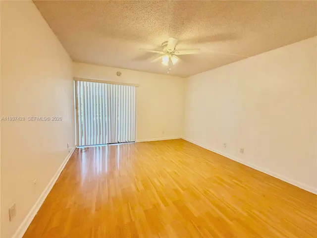an empty room with wooden floor fan and windows