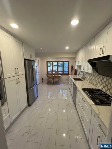 a kitchen with stainless steel appliances granite countertop a refrigerator a sink a stove top oven a counter space and cabinets