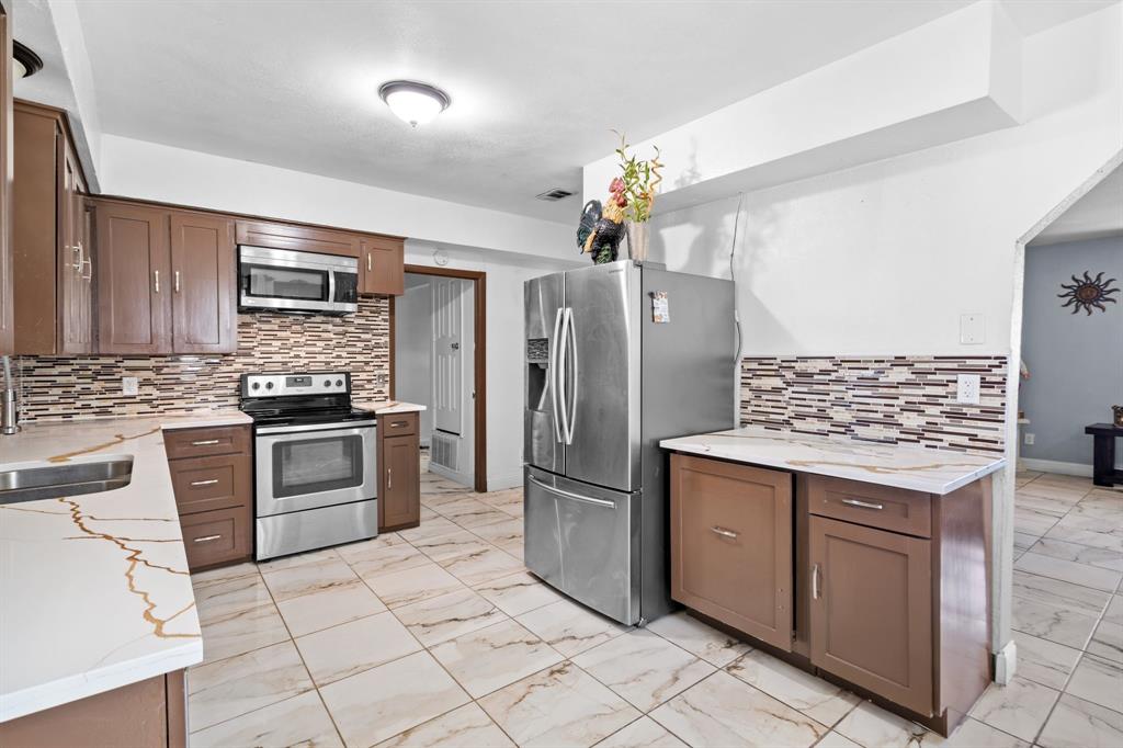 2133 Pleasant Drive Dallas, TX 75227 - Photo 10 of 40 Kitchen featuring appliances with stainless steel finishes, light stone counters, light marble finish flooring, and backsplash