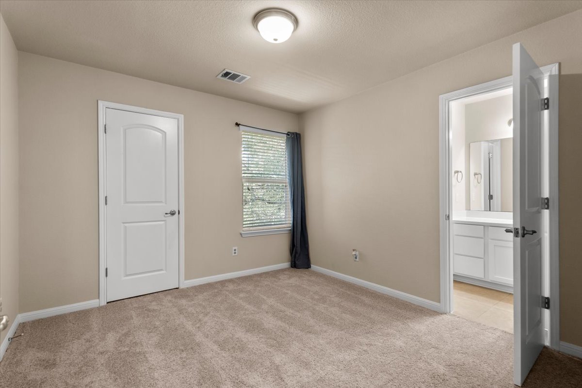 3451 Mayfield Ranch Boulevard, Unit 311 Round Rock, TX 78681 - Photo 26 of 40 Carpeted room featuring a ceiling light fixture, neutral wall paint, a window with blinds and dark drapes, and an open doorway revealing a bathroom with a white vanity and mirror