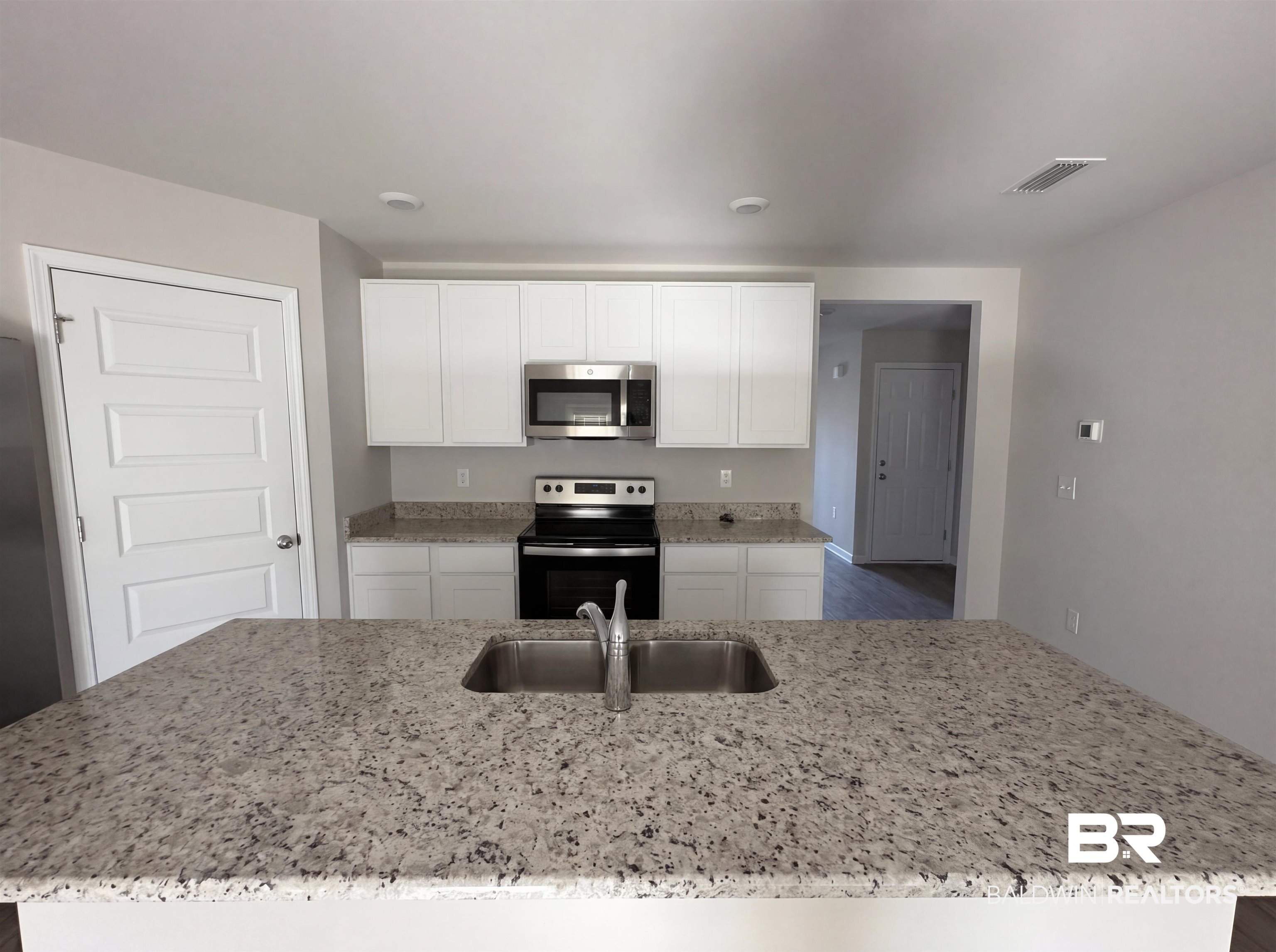 7453 Brompton Drive Foley, AL 36535 - Photo 7 of 15 Kitchen featuring a large central island with an undermount double basin stainless steel sink, solid surface countertops, white shaker-style cabinetry, and stainless steel appliances