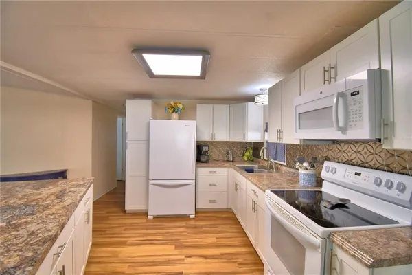 a kitchen with stainless steel appliances kitchen island granite countertop a refrigerator a stove a sink and white cabinets with wooden floor