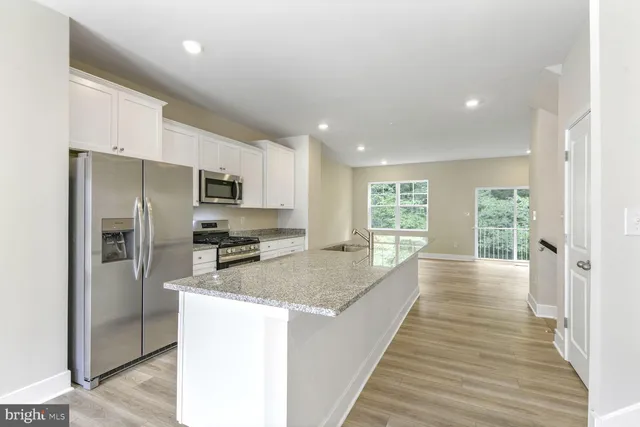 a large kitchen with a center island wooden floor stainless steel appliances and windows