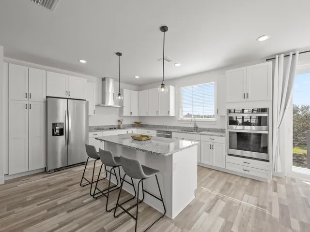 a kitchen with stainless steel appliances a stove a sink dishwasher a refrigerator white cabinets and wooden floor