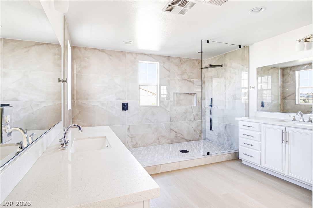 2182 Trivero Street Henderson, NV 89044 - Photo 1 of 50 Gleaming stone tile walls surround a glass-enclosed shower alongside modern dual vanities.
