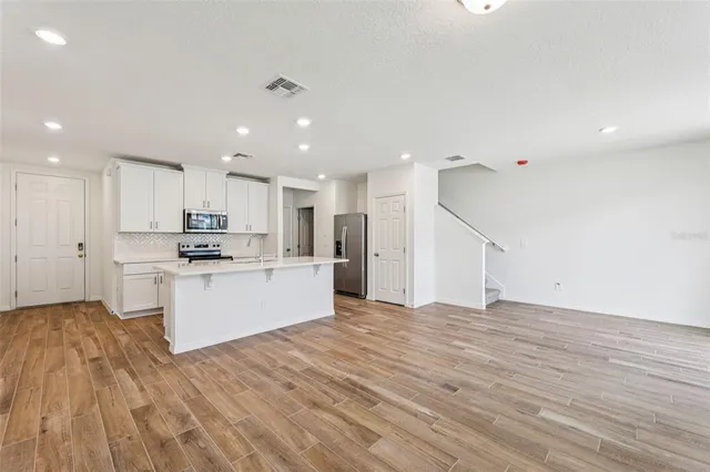 a large white kitchen with kitchen island a sink a stove a refrigerator and white cabinets with wooden floor