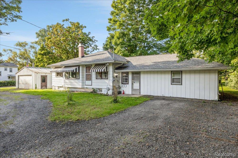 59380 10 Mile Road South Lyon, MI 48178 - Photo 50 of 53 White siding exterior with a pitched roof, front entry door with striped awning, and a detached garage