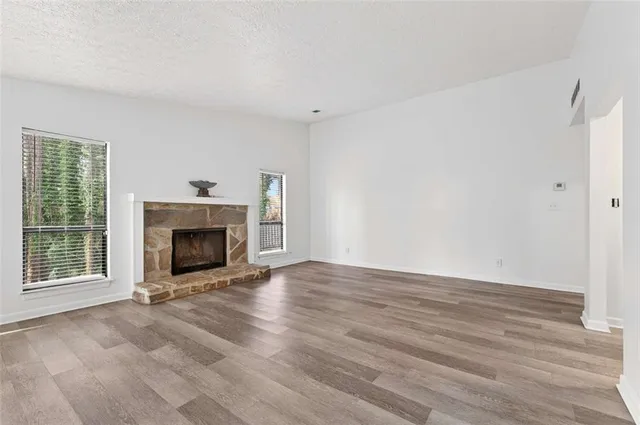 a view of an empty room with wooden floor fireplace and a window