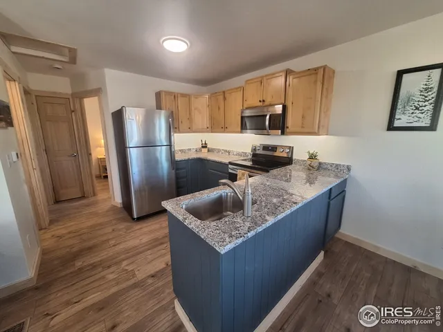 a kitchen with stainless steel appliances granite countertop a refrigerator a stove and a sink with wooden floors