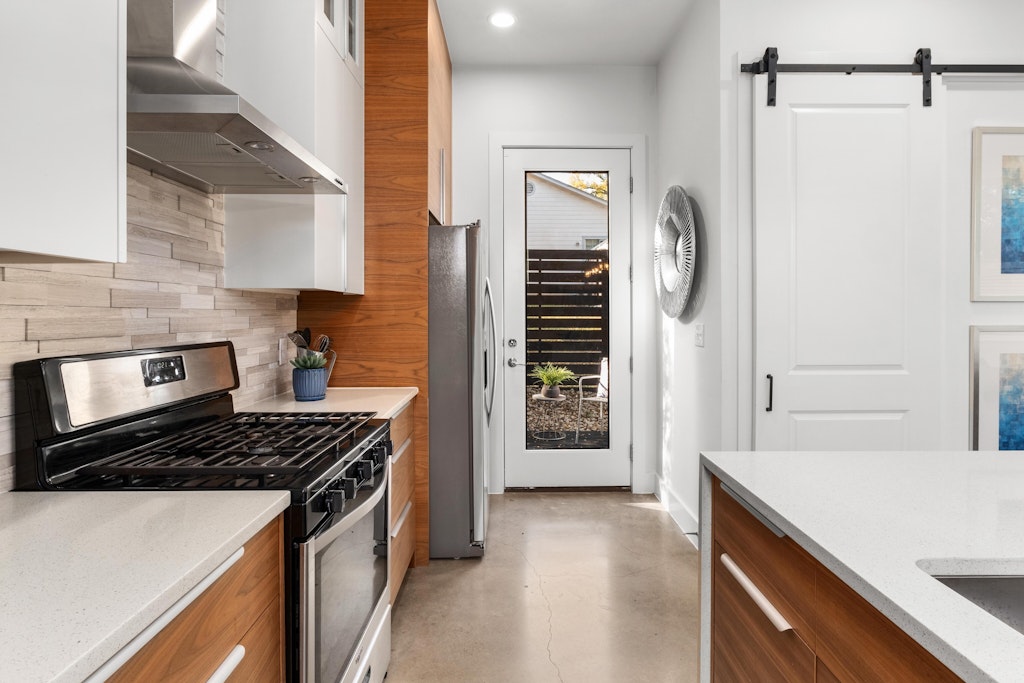 2909 East 13th Street, Unit 2 Austin, TX 78702 - Photo 9 of 23 Kitchen with stainless steel appliances, light stone counters, finished concrete floors, a barn door, and glass insert cabinets