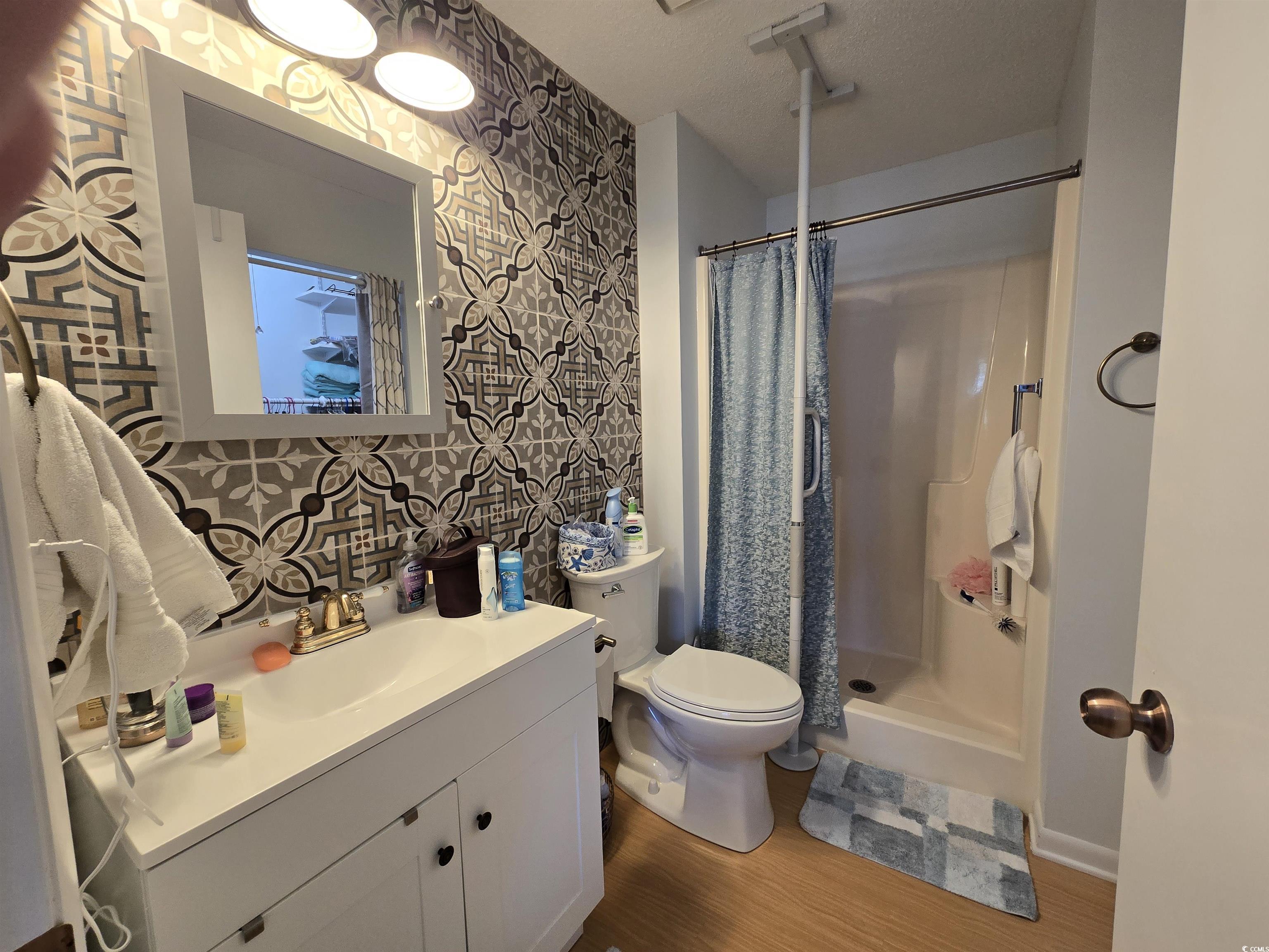 5001 Little River Road, Unit E108 Myrtle Beach, SC 29577 - Photo 12 of 25 Full bathroom featuring a shower stall, wood finished floors, vanity, and wallpapered walls