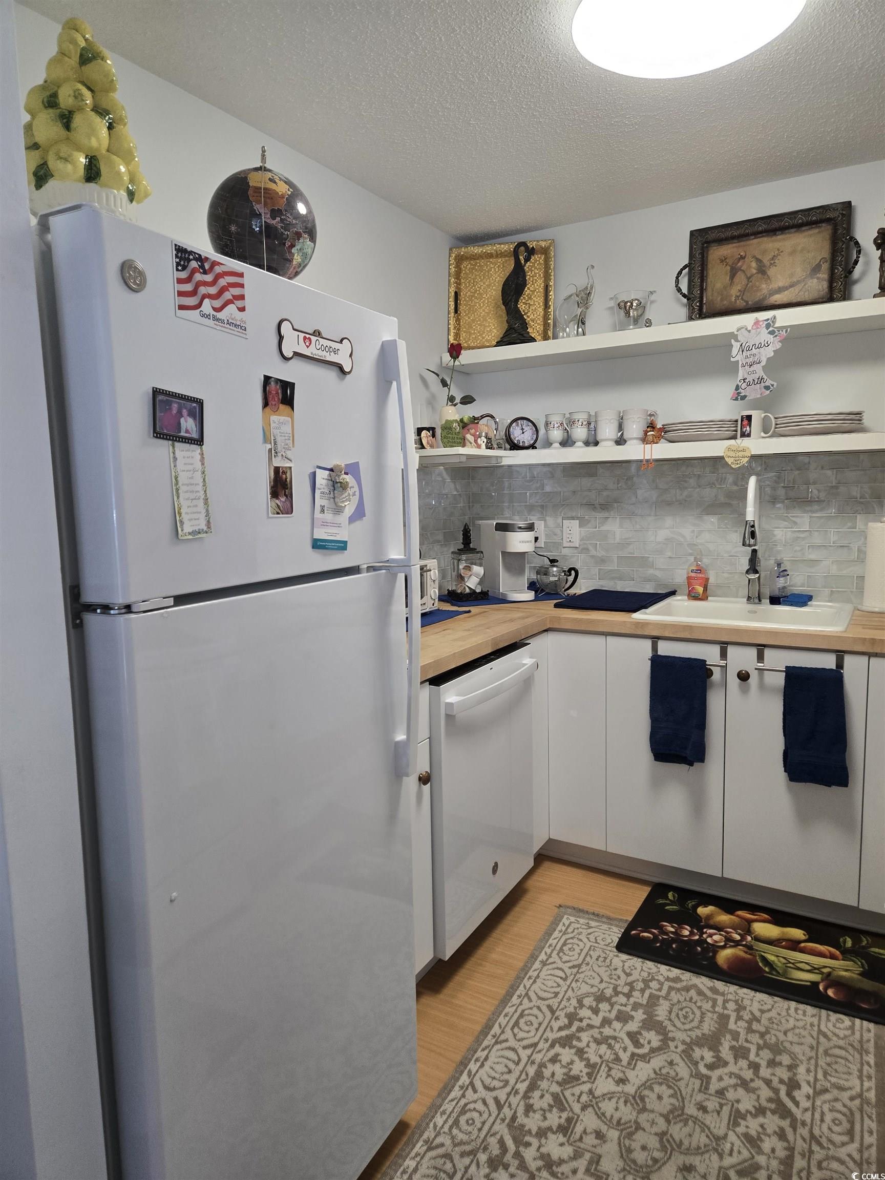 5001 Little River Road, Unit E108 Myrtle Beach, SC 29577 - Photo 6 of 25 Kitchen featuring white cabinets, a textured ceiling, white appliances, light wood finished floors, and backsplash
