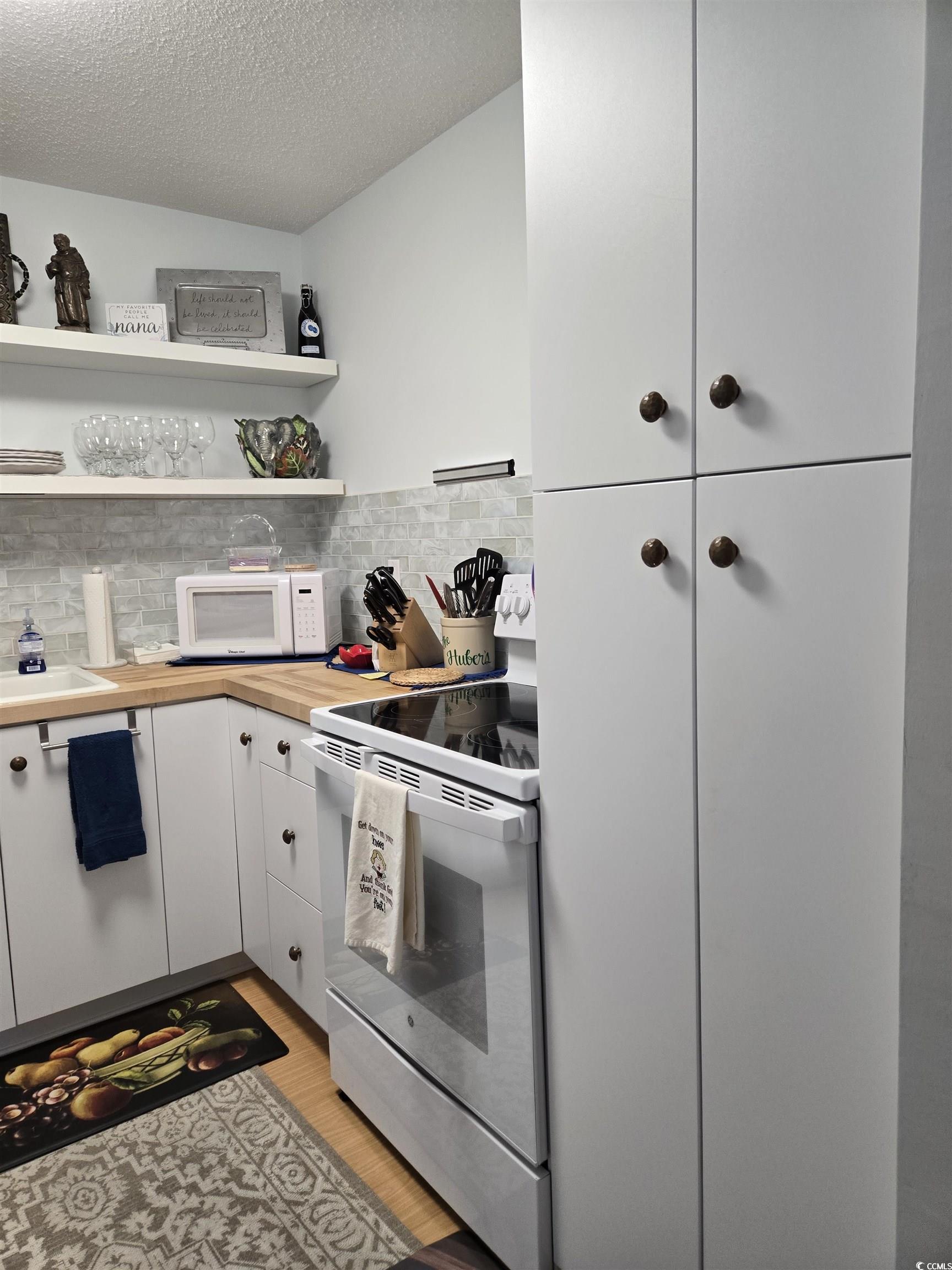 5001 Little River Road, Unit E108 Myrtle Beach, SC 29577 - Photo 7 of 25 Kitchen with white appliances, white cabinets, a textured ceiling, open shelves, and light wood-type flooring