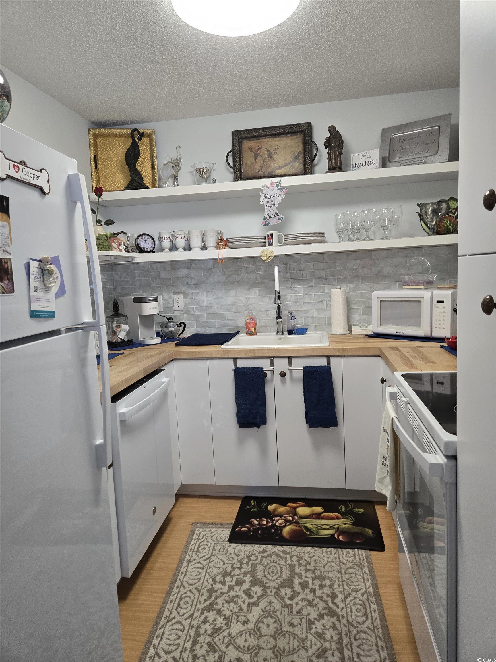 5001 Little River Road, Unit E108 Myrtle Beach, SC 29577 - Photo 8 of 25 Kitchen with white cabinets, white appliances, a textured ceiling, light wood-type flooring, and backsplash