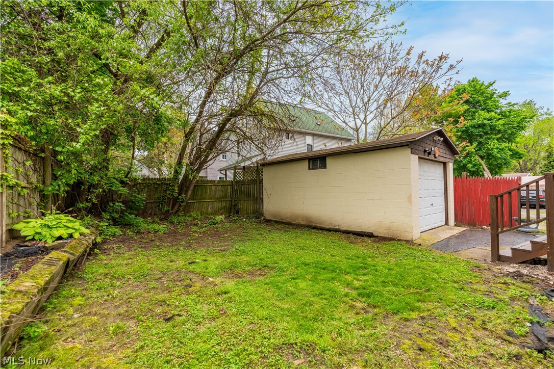 796 Dayton Street Akron, OH 44310 - Photo 23 of 25 Rear exterior featuring a detached garage with an overhead door, a wooden fence, mature trees, and a grassy lawn