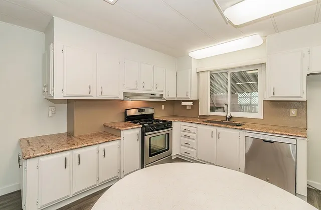 a kitchen with granite countertop white cabinets white appliances a sink and a window
