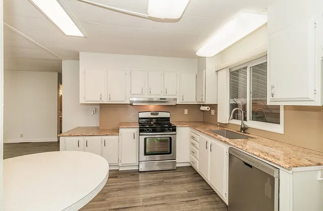 a kitchen with stainless steel appliances granite countertop a stove a sink and white cabinets