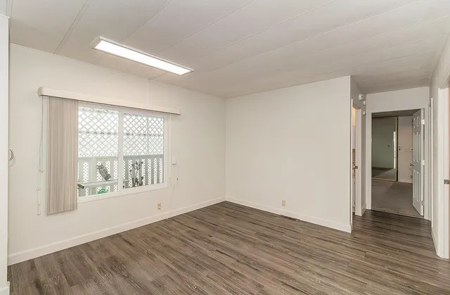 a view of an empty room with wooden floor and a window