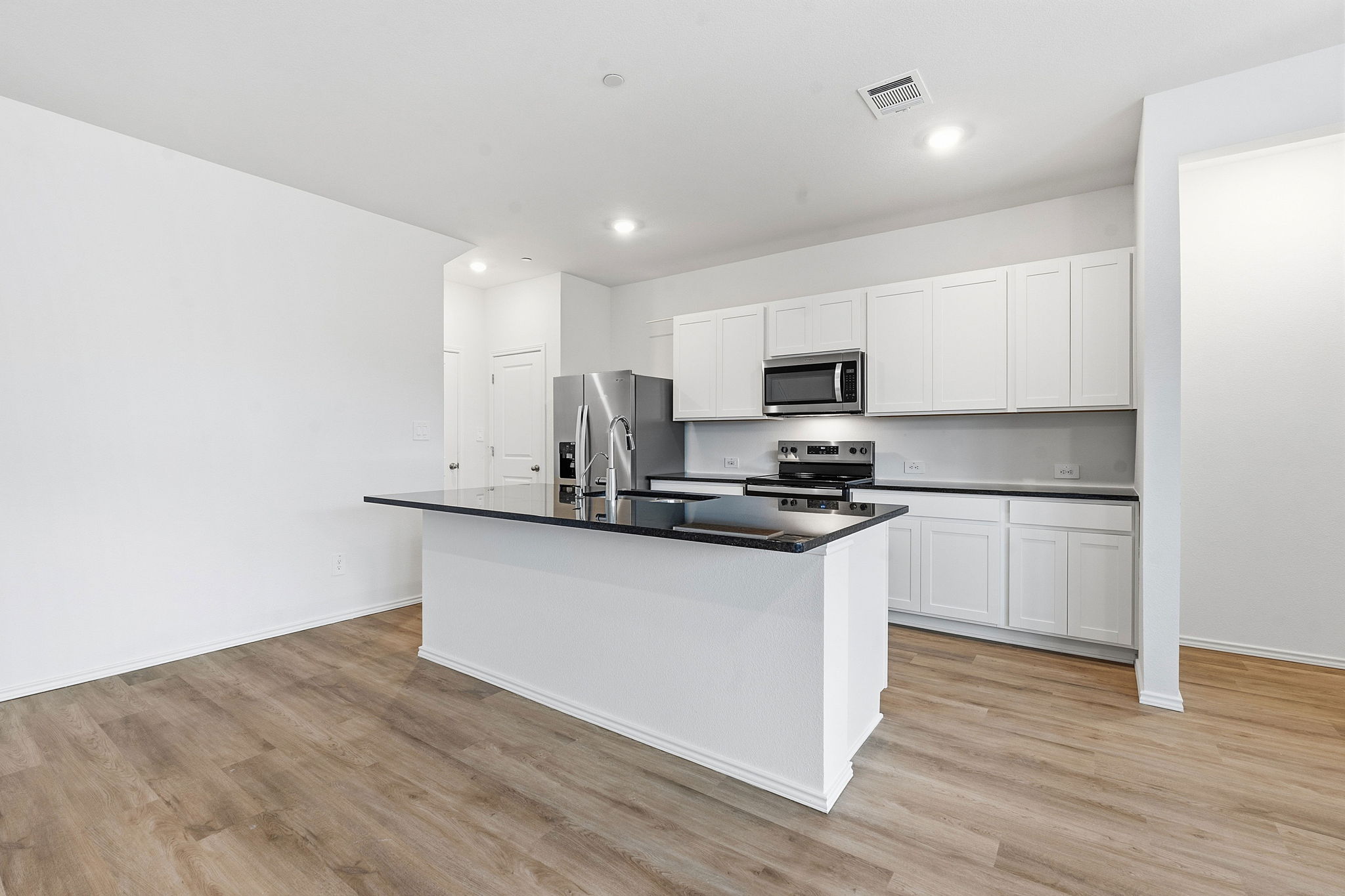 164 Cinnabar Lane, Unit 2 Kyle, TX 78640 - Photo 5 of 21 Open-concept kitchen featuring an island with a black countertop, white shaker-style cabinetry, stainless steel appliances, and wood-finish flooring
