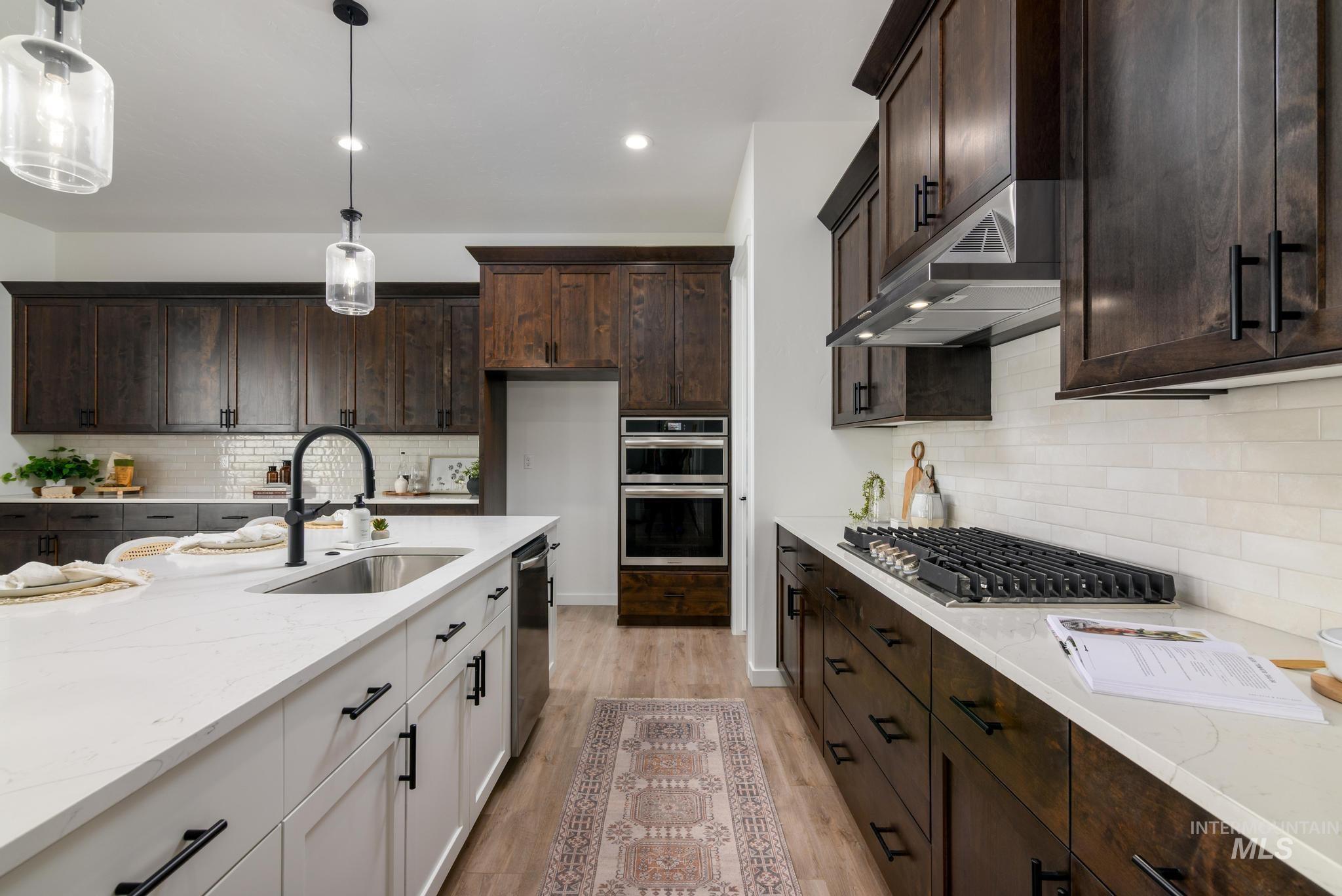 15086 Steel Cloud Avenue Caldwell, ID 83607 - Photo 12 of 41 Kitchen featuring appliances with stainless steel finishes, under cabinet range hood, light stone counters, light wood finished floors, and dark brown cabinetry