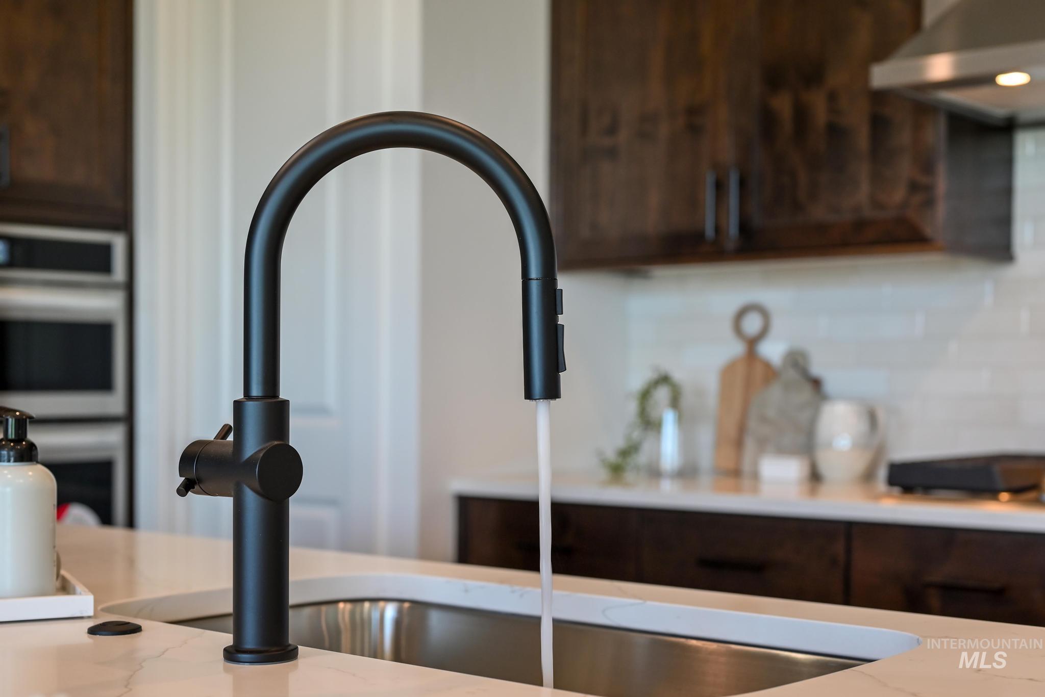 15086 Steel Cloud Avenue Caldwell, ID 83607 - Photo 16 of 41 Kitchen view of under cabinet range hood, dark brown cabinetry, double oven, and decorative backsplash
