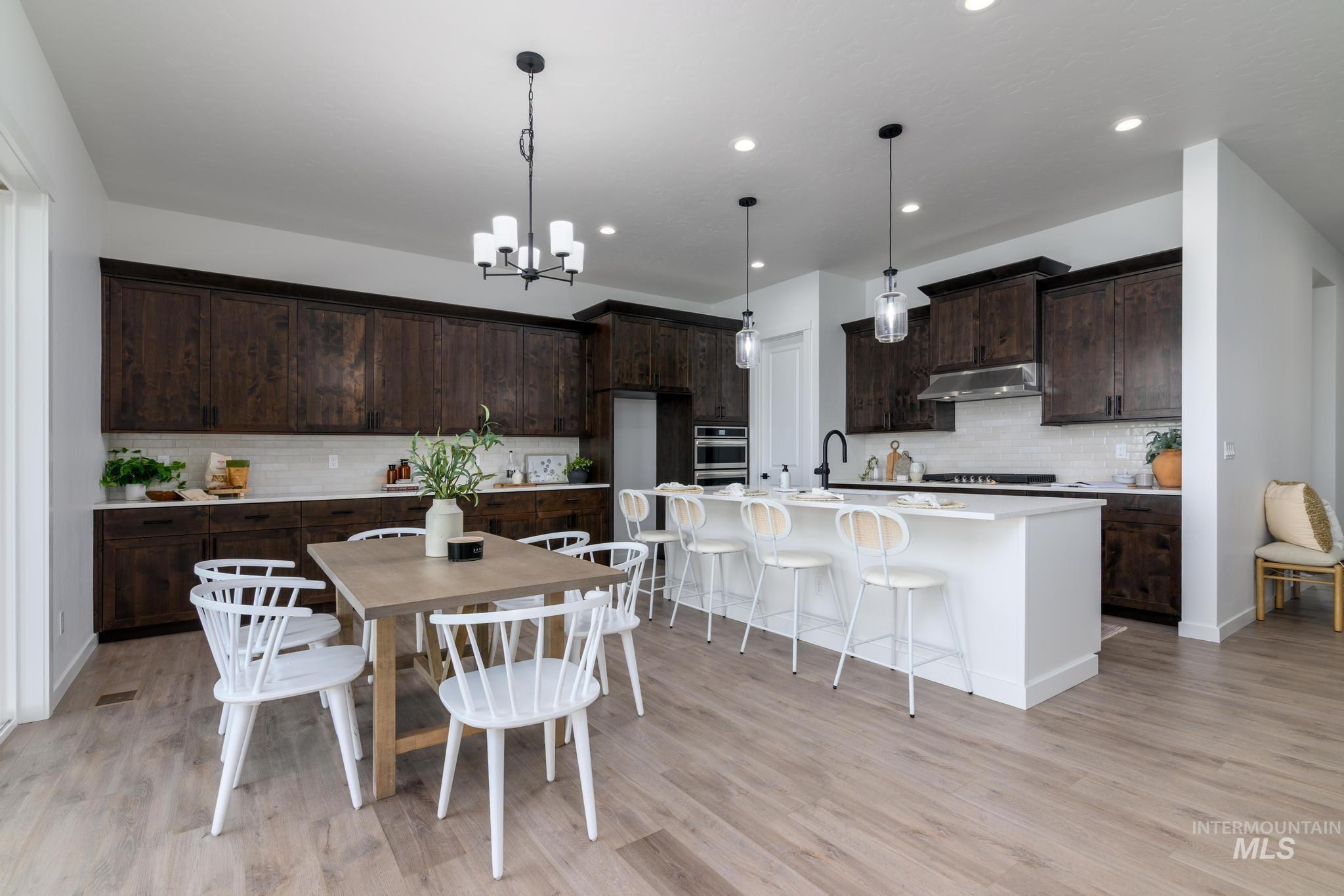 15086 Steel Cloud Avenue Caldwell, ID 83607 - Photo 10 of 41 Kitchen with ventilation hood, decorative backsplash, dark brown cabinets, a chandelier, and light wood-type flooring